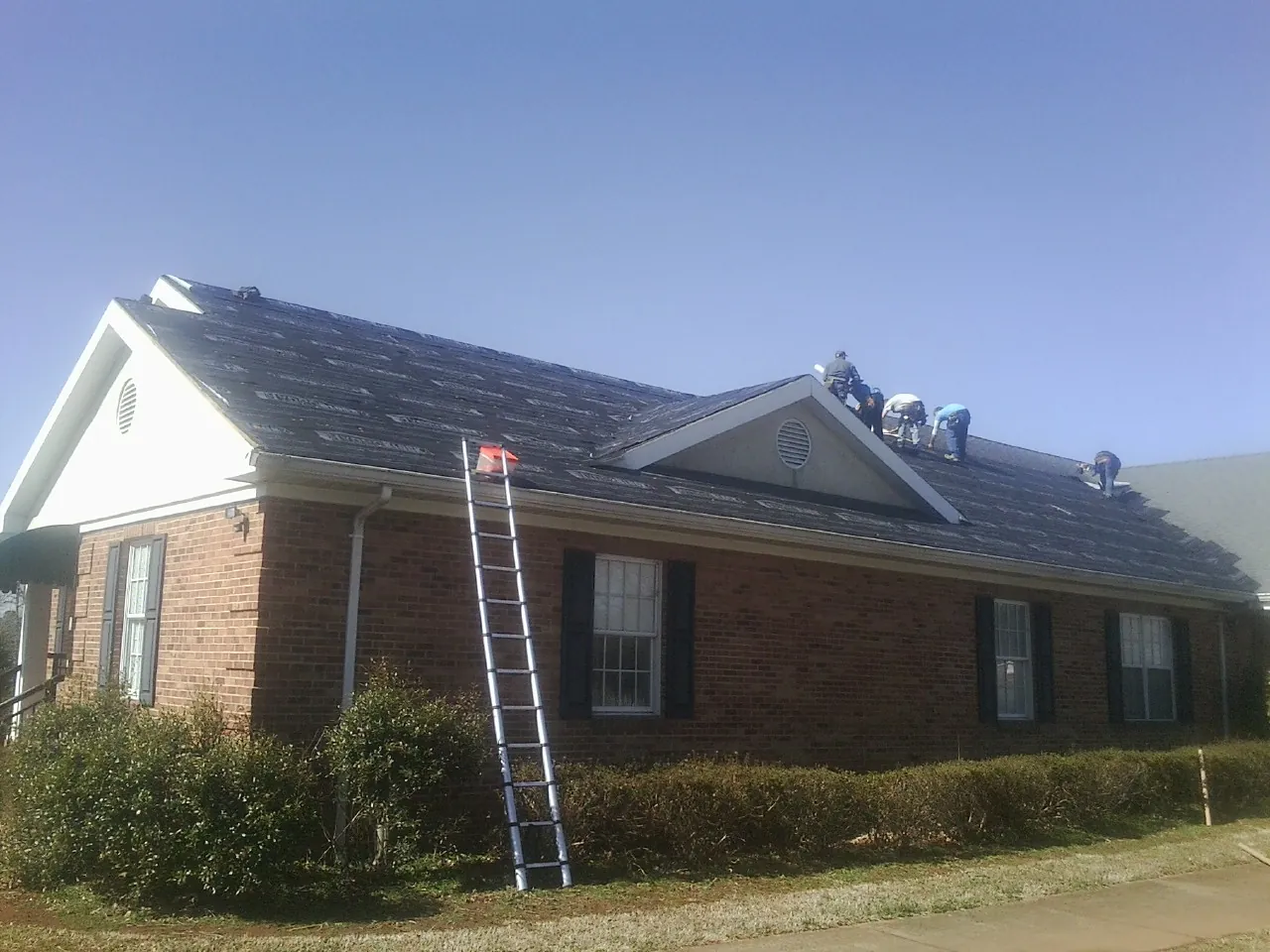 Crew tearing shingles off a brick ranch roof with a ladder set — Emergency Roof Repair work by our crew in Stoughton