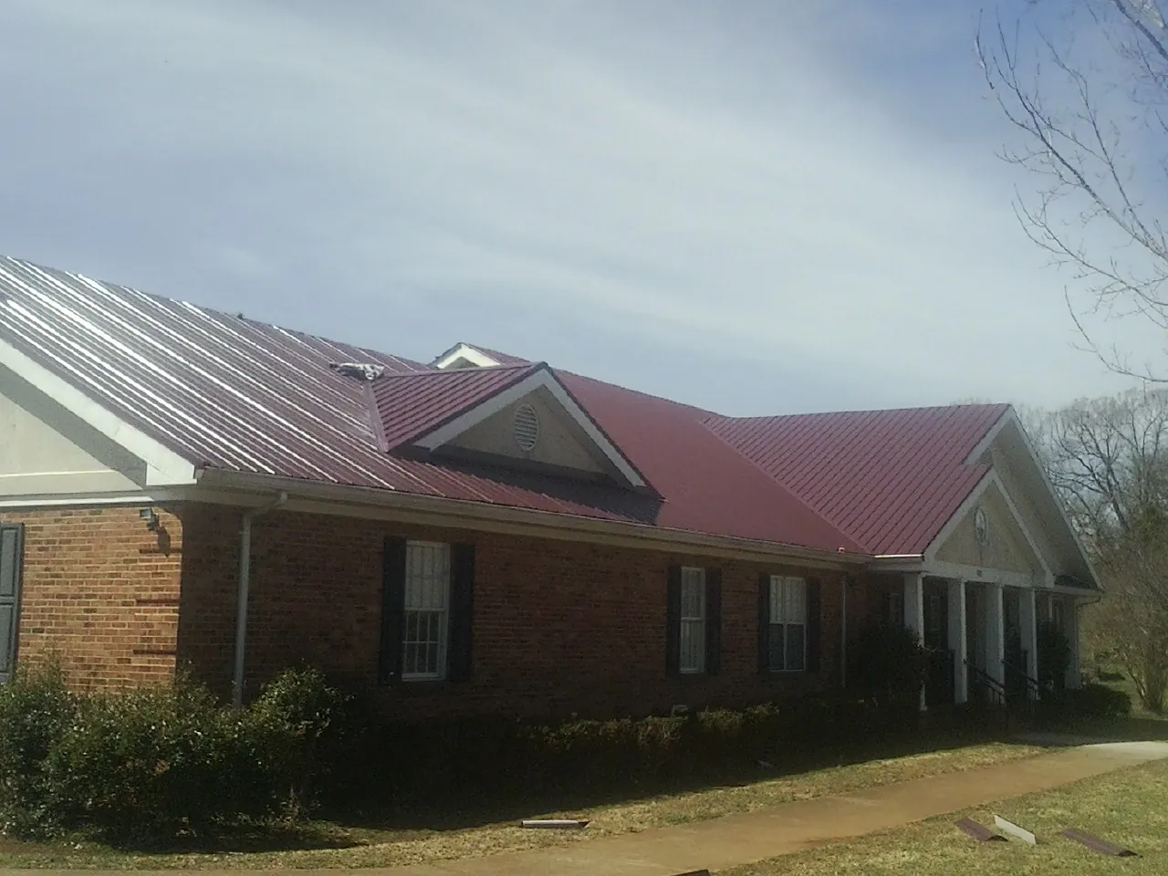 Red metal roof with gabled entries on a long brick building, from a Hail Damage Roof Repair job in Stoughton