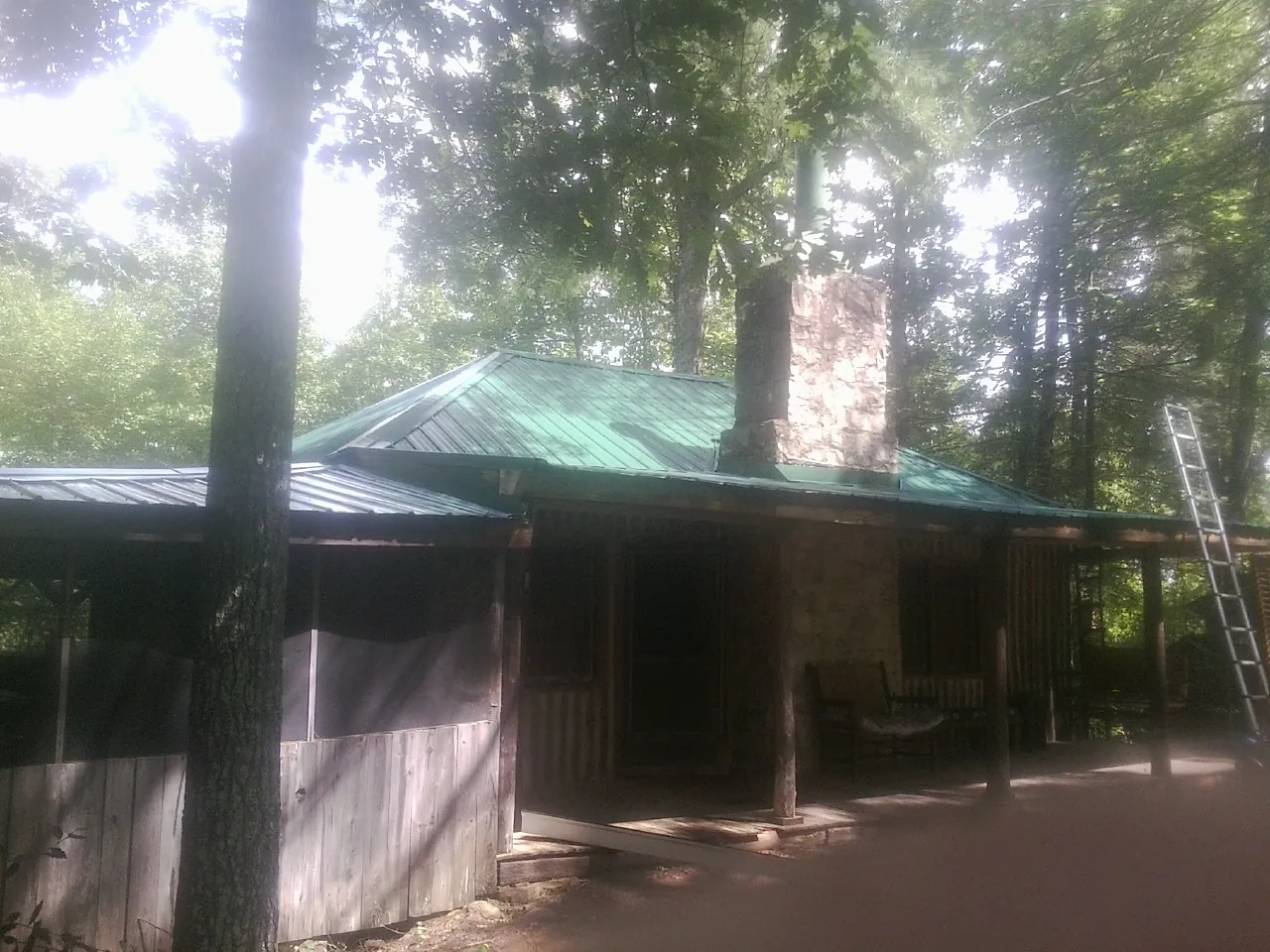 Green metal roof and stone chimney above a log cabin porch in Stoughton