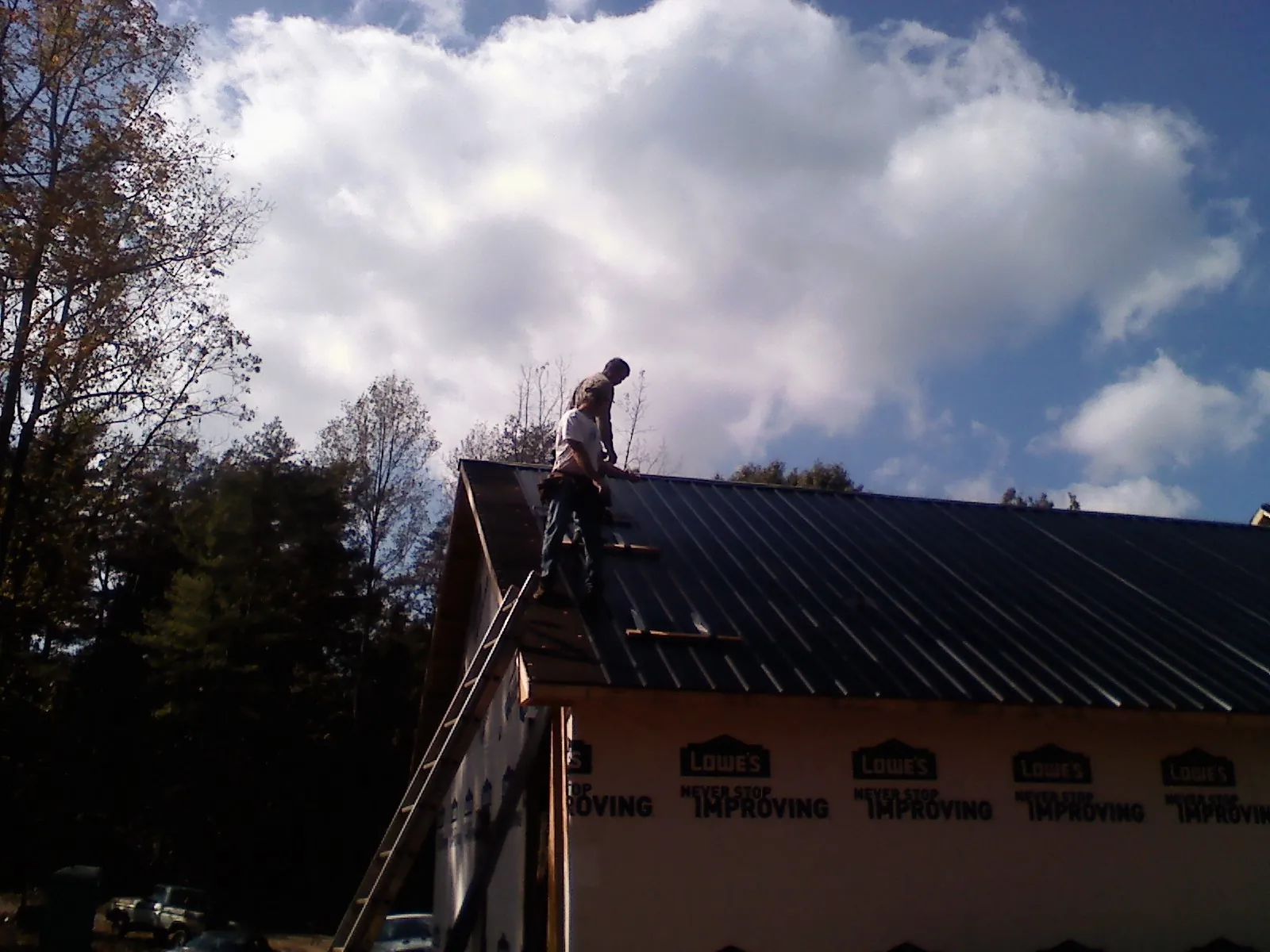 Roofer fastening dark metal panels high against a cloudy sky, from a Roof Inspection job in Stoughton