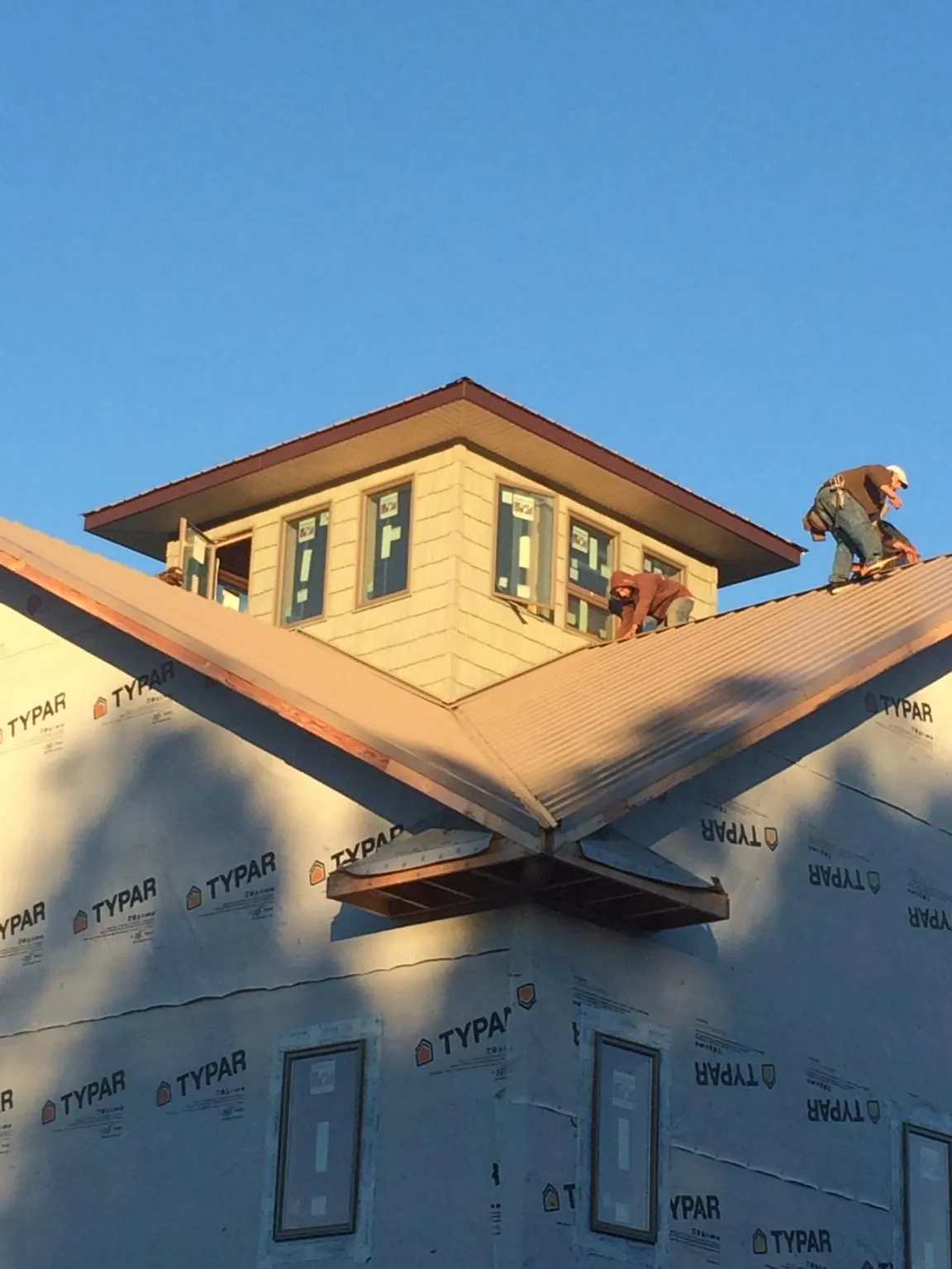 Roofers working around a rooftop cupola on a new metal roof at sunset — Roof Waterproofing in Stoughton by Roofing Brothers
